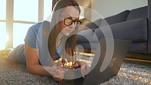 Woman with glasses is lying on the floor and makes an online purchase using a credit card and laptop. Online shopping