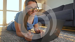 Woman with glasses is lying on the floor and makes an online purchase using a credit card and laptop. Online shopping