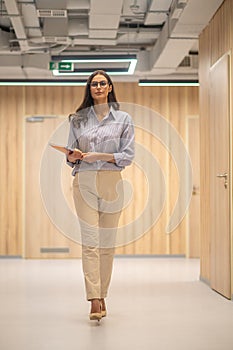 Woman in glasses with notebooks walking down corridor