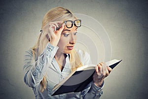 Woman with glasses reading looking at book shocked surprised