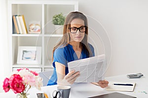 Woman in glasses reading newspaper at office