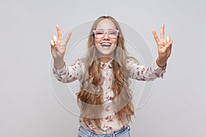 Woman in glasses showing v sign with fingers, peace or victory gesture, rejoicing success.