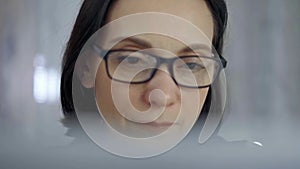 Woman with glasses sipping from a white mug while sitting and looking into laptop monitor. Front view and close up