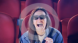 A woman in glasses in smiling while watching a movie