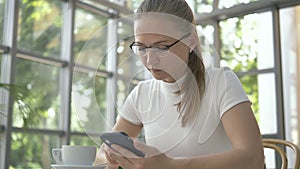 Woman with glasses surfs internet with mobile phone in cafe