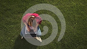 Woman in glasses typing on her laptop on grass