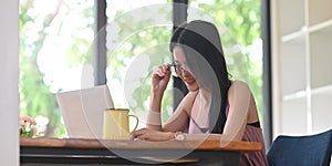 A woman with glasses is using a computer laptop while sitting at the wooden working desk