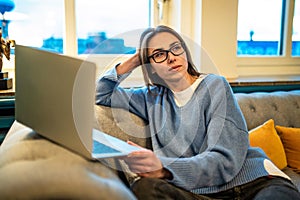 Woman in glasses using laptop for internet browsing or working online sitting sofa