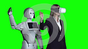 Woman with glasses of virtual reality raises has hand up and waves the robot repeats after her. Green screen. Slow