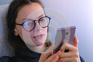 Woman in glasses watches serial on mobile phone. Face close-up.