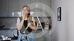 woman with glasses wearing a black sleevless shirt and holding a hammer, thinking about repair