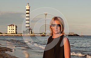 Woman with glasses who is photographed on the beach with a lighthouse behind her for navigators. photo taken on the beaches betwe