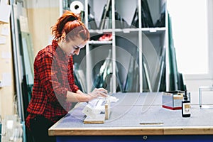 Woman glazier worker sticking together glass panes with ultraviolet lamp