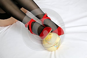 Woman with globe, sexy girl in black stockings and red shoes lies on the bed