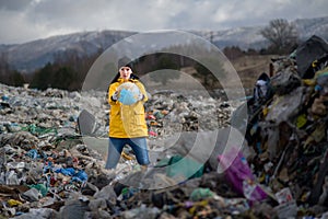 Woman with globe standing on landfill, environmental concept.