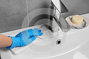 Woman in glove cleaning sink with paper towel, closeup