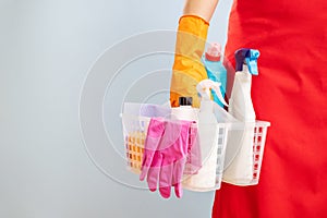 Woman in gloves and apron holding basket with sponge and cleaning products