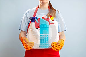 Woman in gloves and apron holding basket with sponge and cleaning products