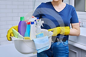 Woman in gloves with basin of detergents in bathroom