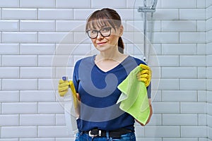 Woman in gloves with detergent spray washcloth doing cleaning in bathroom