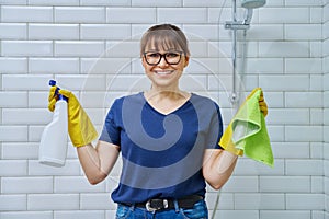 Woman in gloves with detergent spray washcloth doing cleaning in bathroom