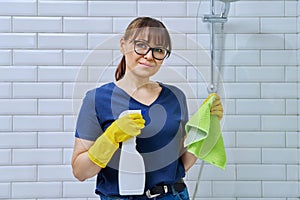 Woman in gloves with detergent spray washcloth doing cleaning in bathroom