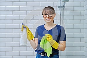 Woman in gloves with detergent spray washcloth doing cleaning in bathroom