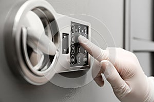 Woman in gloves entering code on keypad of safe, closeup