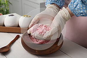 Woman in gloves making bath bomb mixture at white table indoors, closeup