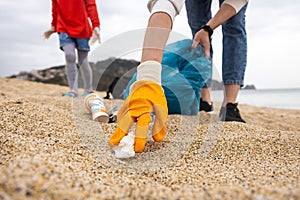 A woman in gloves with a special blue bag picks up garbage among the sand along the coast. The problem of environmental