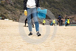 A woman in gloves with a special blue bag picks up garbage among the sand along the coast. The problem of environmental