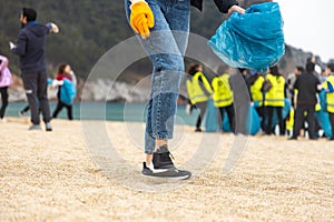 A woman in gloves with a special blue bag picks up garbage among the sand along the coast. The problem of environmental