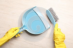 Woman in gloves sweeping wooden floor with plastic whisk broom and dustpan, top view