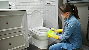 Woman in gloves using cleaning detergent clean toilet in bathroom