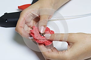 A woman glues a metal hairpin to a knitted brooch in the form of a flower.