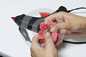 A woman glues a metal hairpin to a knitted brooch in the form of a flower.