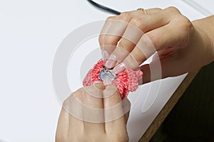 A woman glues a metal hairpin to a knitted brooch in the form of a flower.