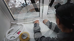 Woman glues a sealing rubber tape on a window