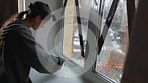 Woman glues a sealing rubber tape on a window