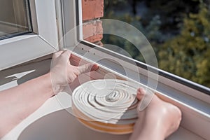 a woman glues a sealing rubber tape on a window in a living room