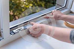 a woman glues a sealing rubber tape on a window in a living room