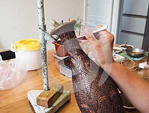 Woman gluing tiny shaped cloisonne wires to a copper vase creating a intricately constructed pattern for a enamel cloisonne