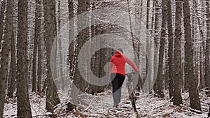 The woman goes with bicycle on a path in the wood. Women in an orange jacket walks with a dog. Sporty girl riding a bike