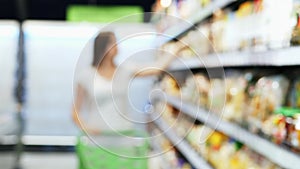 Woman goes to camera in blur through the store with green shopping trolley, between the shelves, choose goods