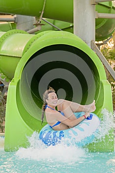 woman going down a water slide. happy woman going down on the rubber ring by the orange slide in the aqua park. Summer Vacation.