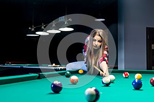 Woman going hit a ball with cue in billiard.