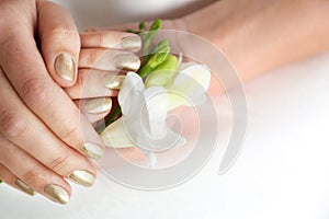 Woman with gold manicure holding flower on light background. Nail polish trends