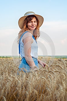 Woman with golden brown hair in fashionable hat. Beautiful golden wheat field with ripe spikelets. Happy girl enjoying