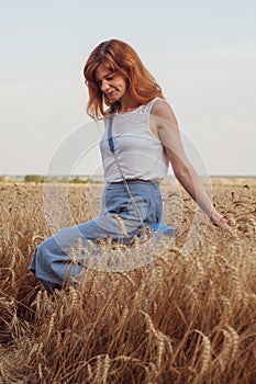 Woman with golden brown hair walks through beautiful golden wheat field, hot summer season. Happy girl enjoying life