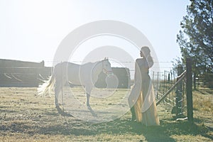 Woman in golden dress next to white horse